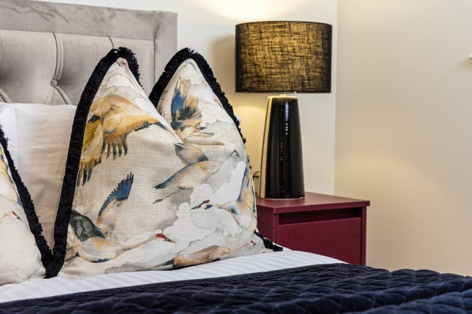 Luxury Airbnb bedroom with decorative cushion and modern bedside lamp.
